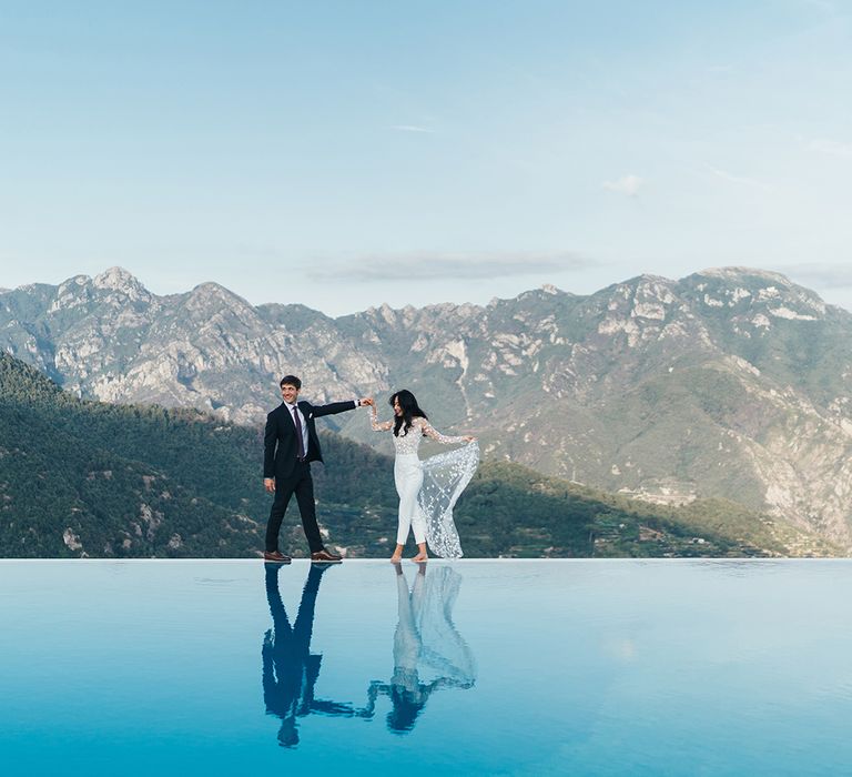 Bride in a Rime Arodaky jumpsuit with lace train dancing near an infinity pool