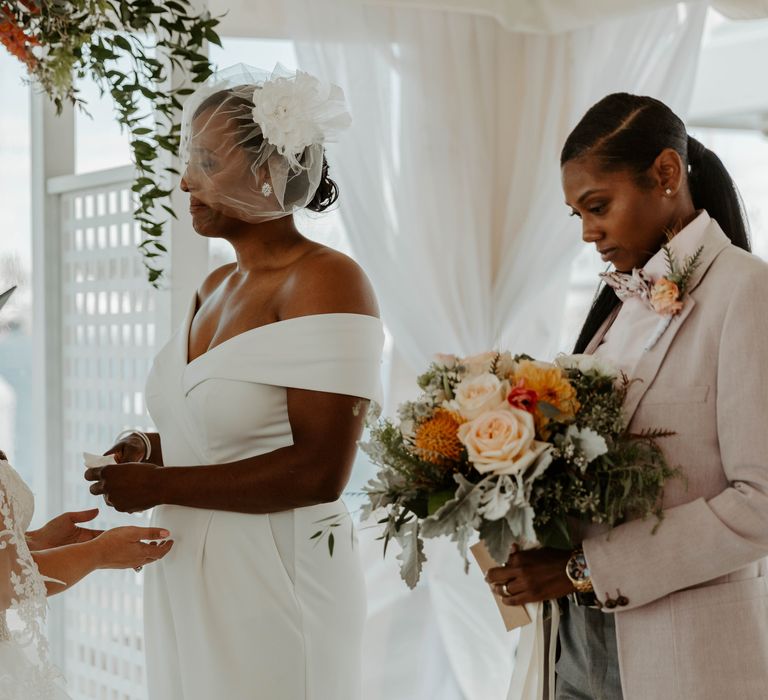 Best person holding the orange, coral and peach wedding bouquet as the black bride gets emtional during the LGBTQ+ wedding