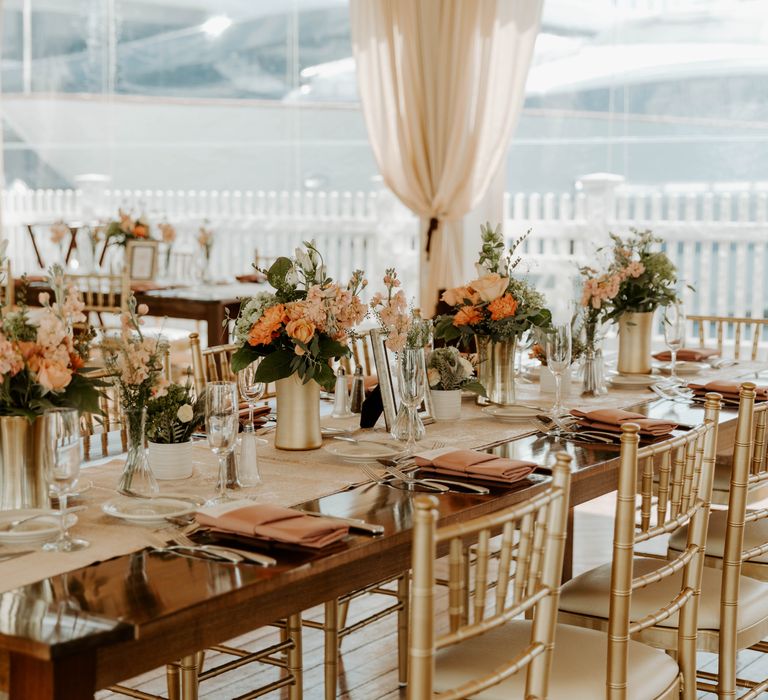 Covid secure wedding reception on a marina dock with gold reception chairs and blush pink and peach wedding flowers 