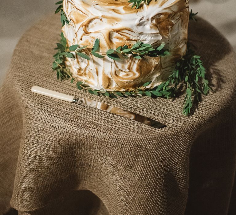 Meringue iced wedding cake decorated with green foliage on a hessian dressed table