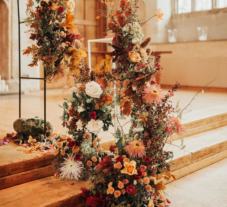 Red and orange autumn wedding flowers decorating the altar flower arch 