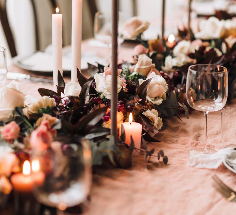 Pink and burgundy wedding flowers and foliage for elegant table runner with taper and pillar candles 