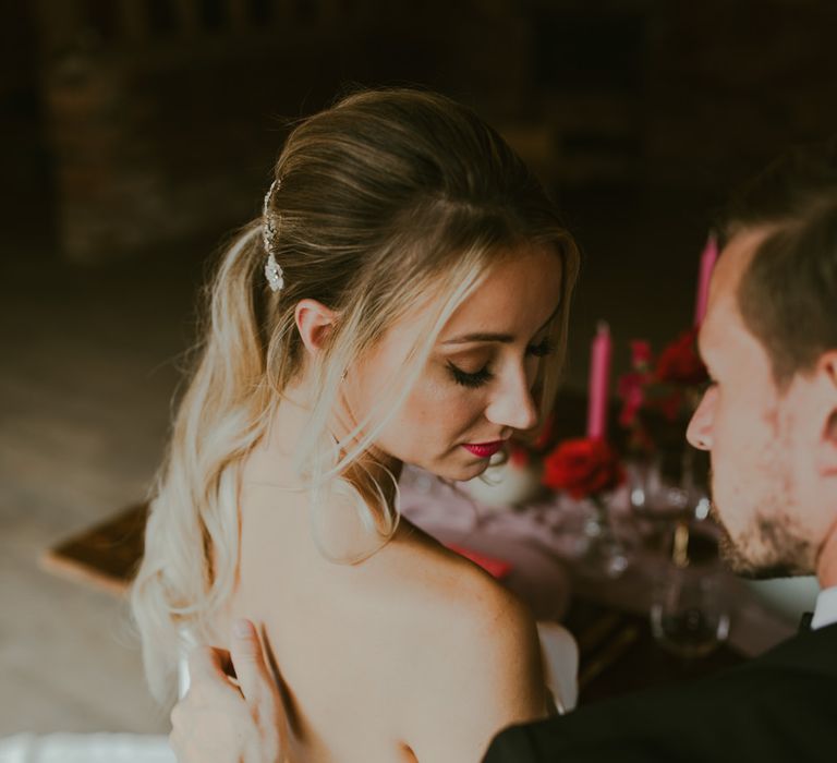 Bride looks down as groom strokes her back