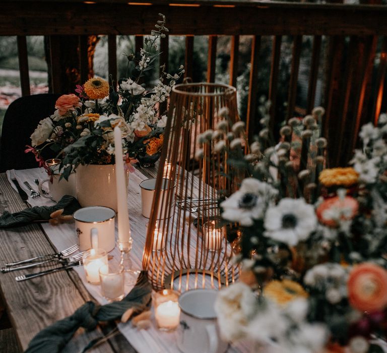 Rustic table setting on wooden table outdoors surrounded by colourful floral arrangements