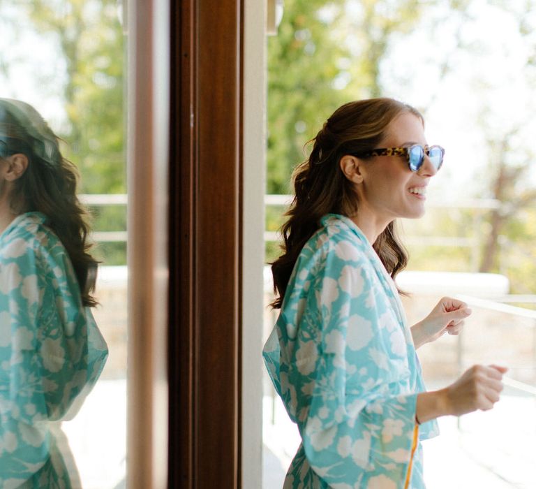 The bride getting ready in the sunshine in a blue dressing gown and sunglasses