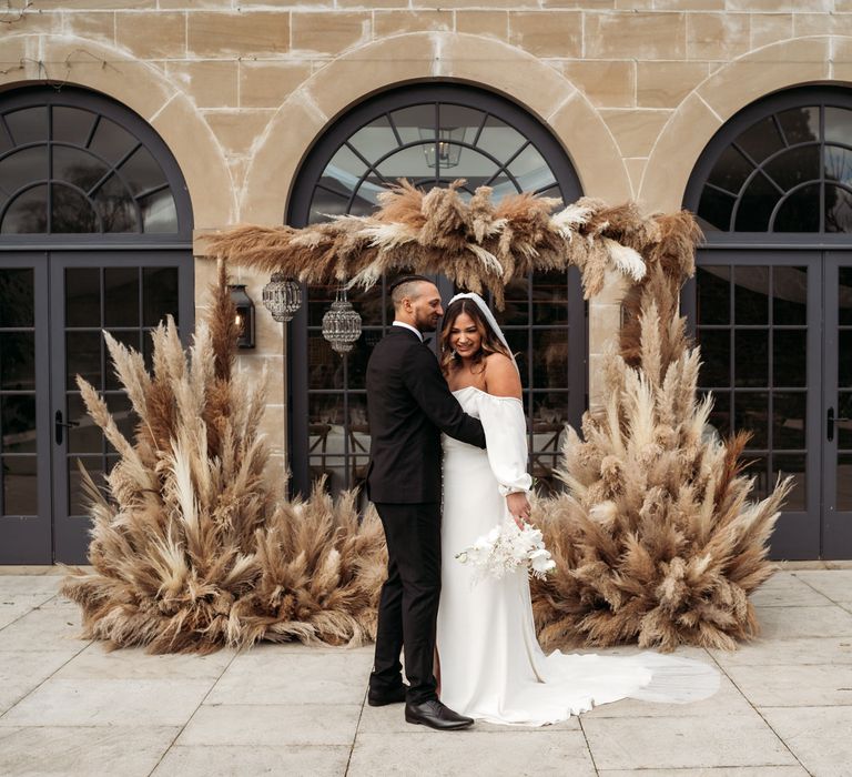 Bride and groom standing in from of Middleton Lodge with a pampas grass installation