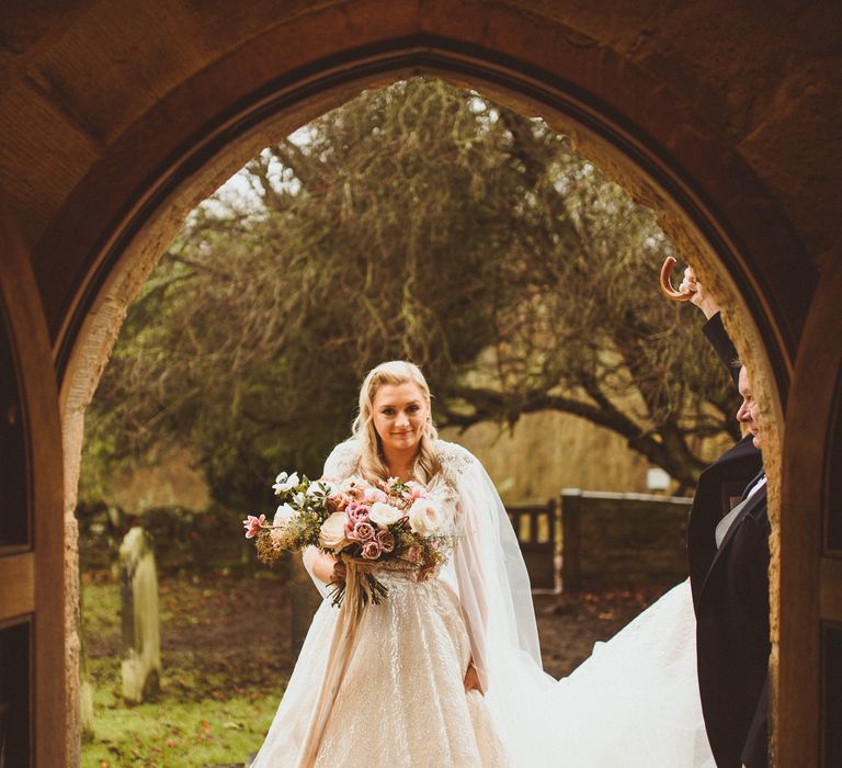 Bride in a princess wedding dress with silver thread holding a blush pink wedding bouquet outside the church 