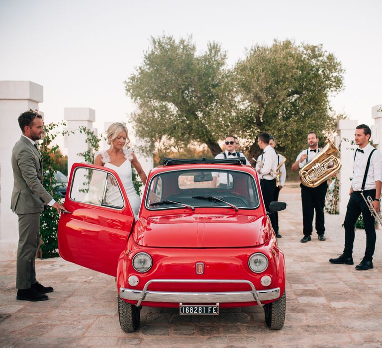 The bride and groom getting into a vintage red Fiat 500 as the band plays