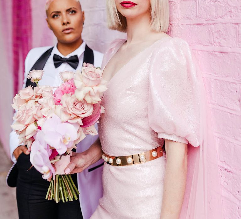 Blonde bride with bobbed hair wearing a shimmering pink jumpsuit with puff sleeves 