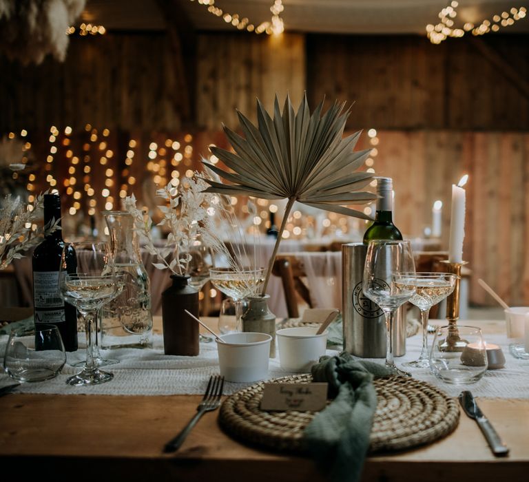 Place setting with wicker place mat, ink wells filled with dried palm leaves and gold candlesticks 