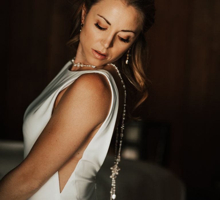 Bride looks across shoulder as she wears long vintage pearl necklace that falls down her back