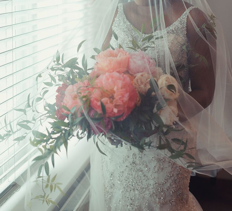 Bride wears veil over her face on her wedding day as she carries floral bouquet