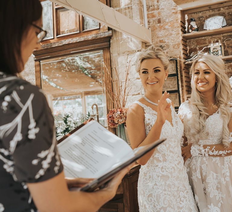 Two brides in white dresses with blonde hair kiss as a guest performs a reading at their wedding at Crab and Lobster Fairytale Wedding.