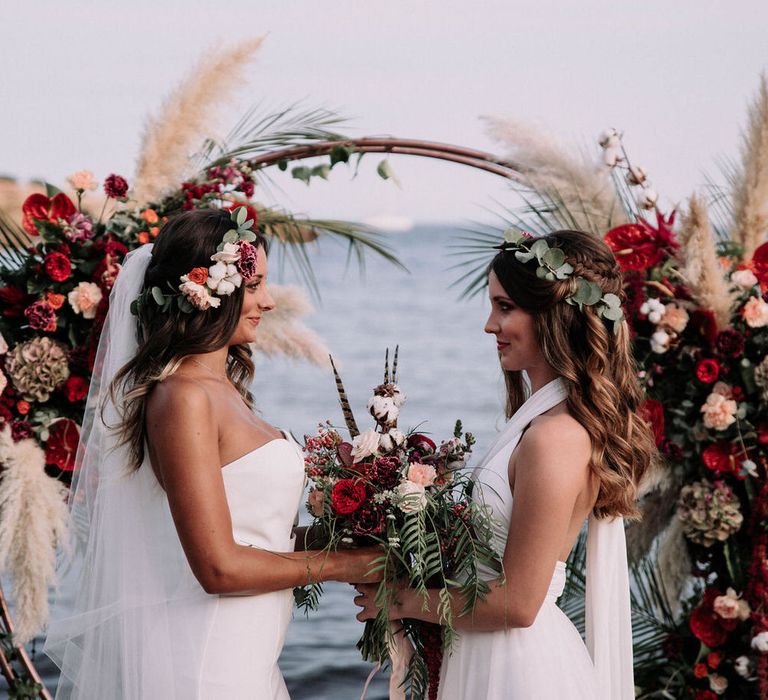 Two brides getting married in Ibiza in front of stunning red and pink romantic florals