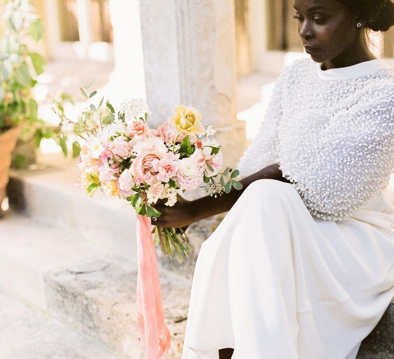 Bride in a sequin wedding dress sitting on some steps exposing her bow Emmy London wedding shoes 