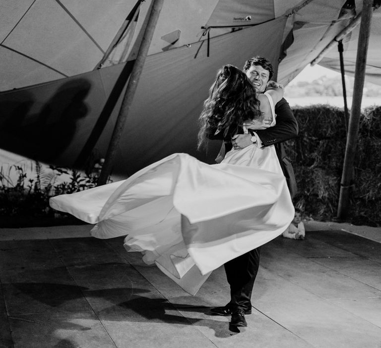 Groom swings around bride in white Elbeth Gillis dress on the dance floor at home farm wedding