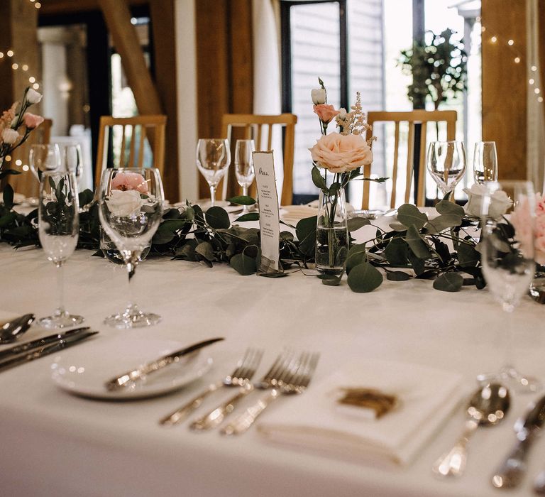 Classic and traditional table scape with white tablecloths and minimal glass vases with roses and green foliage