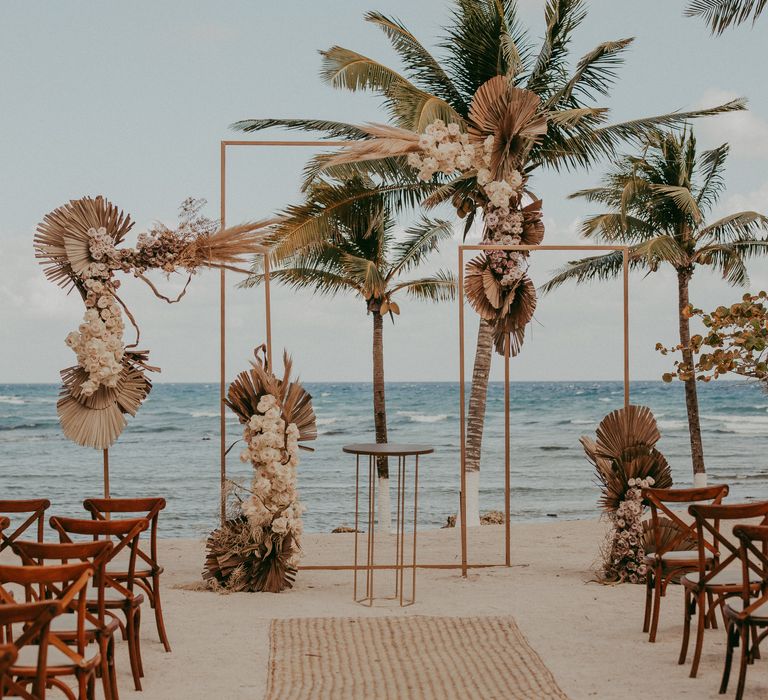 Beach Mexico wedding venue complete with wooden chairs lining the aisle, palm trees and dried floral arrangements