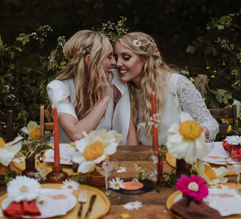 two boho brides with long wavy hair sitting at a sixties decorated wedding reception tablescape