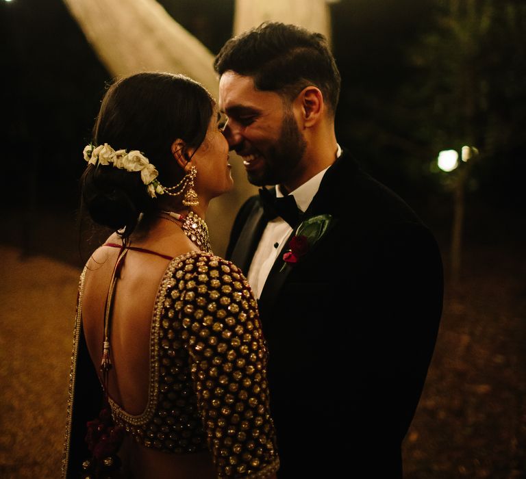 Bride & groom look lovingly at one another as fairy lights hang from the trees outdoors