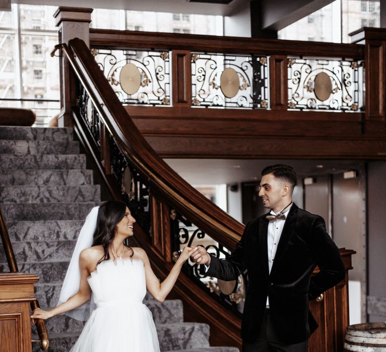 Groom helps bride down from stairs on the day of their wedding 