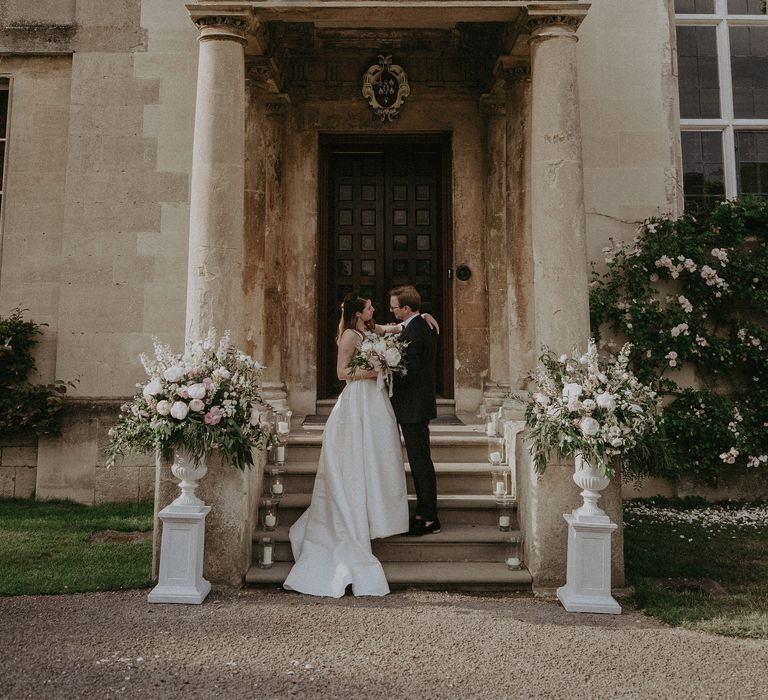 Bride & groom stand in front of large doorway at Elmore court on the day of their wedding