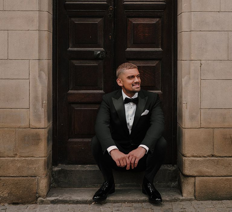 Stylish groom in a black tuxedo with shiny shoes and bow tie 