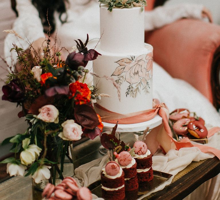 Dessert table with hand painted wedding cake, red velvet mini sandwich cakes, macaroons and glazed doughnuts