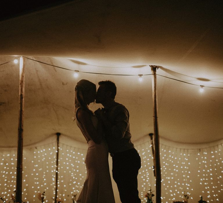 Shadowed image of bride and groom kissing in front of fairy lit tipi