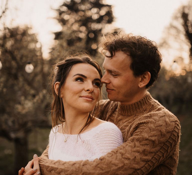 Groom in a brown cable knit jumper embracing his bride in a cashmere jumper during their golden hour portrait session