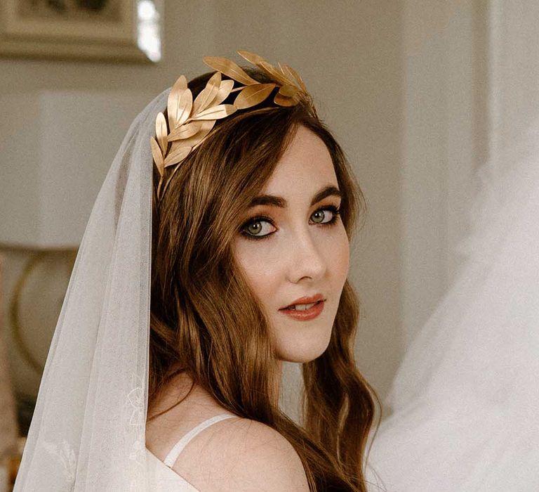 Bride with long auburn hair wearing a gold crown with dark black eyeliner and light brown lipstick wedding makeup 