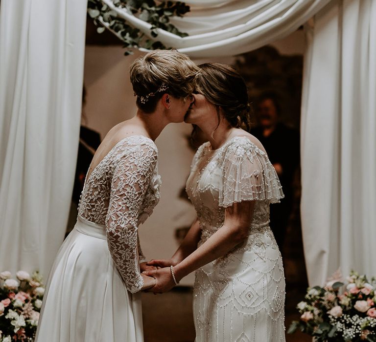 Bride with short hair in a long sleeve wedding dress kissing her bride in an embellished wedding dress at the altar of their Woolas Barn wedding 