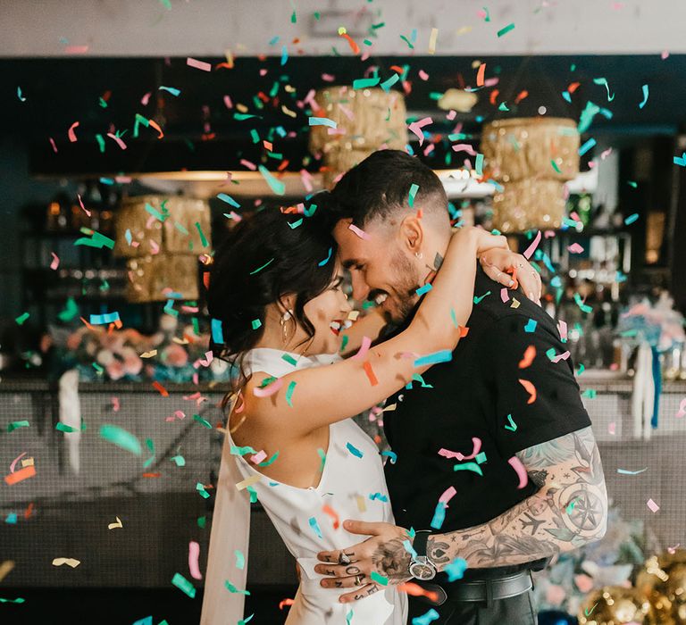 colourful confetti moment with bride in a halterneck wedding dress and red lipstick and groom in a short sleeve black shirt 