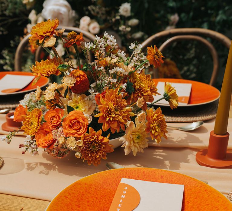 Place setting with orange plate and on the day stationery menu card with orange flower centrepiece decor 