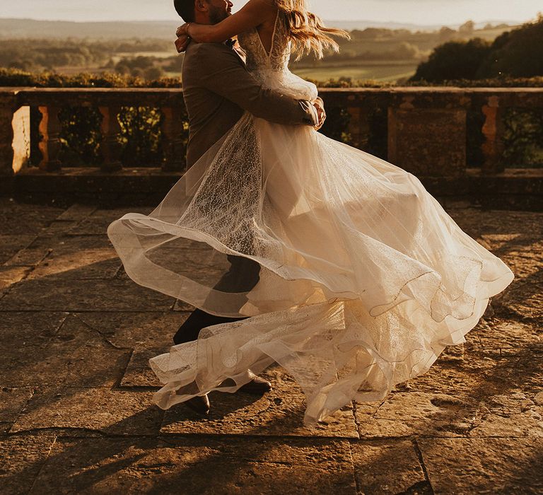 Groom lifts his bride outdoors on their wedding day as the sun begins to set