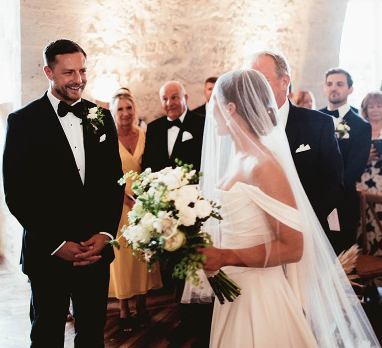 Bride wears Halfpenny London veil across her face whilst carrying classic white bouquet