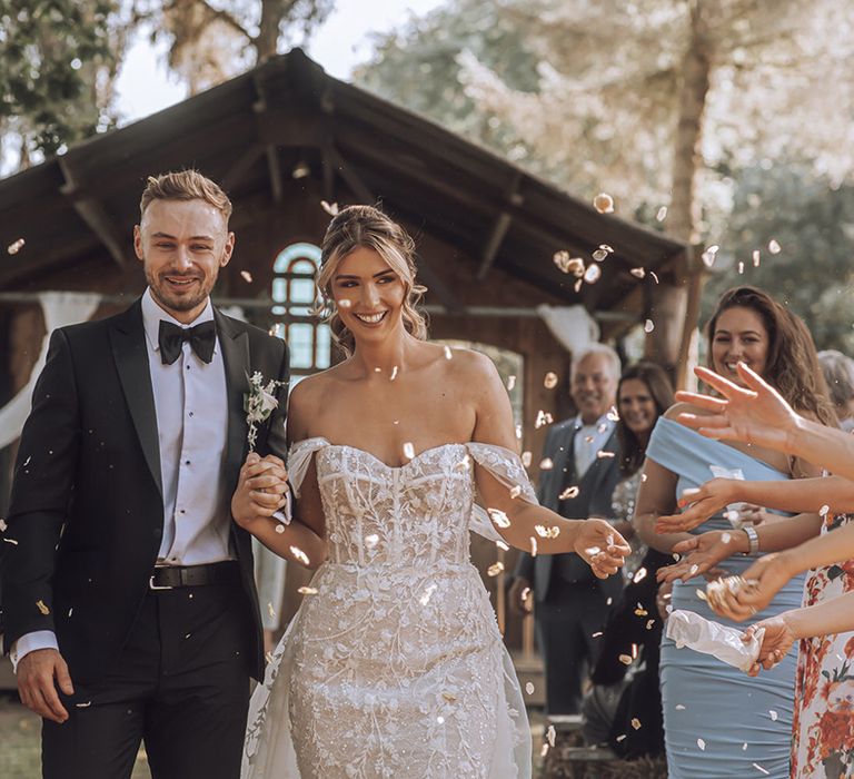 Bride & groom walk down the aisle as confetti is thrown around them 