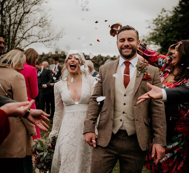 Confetti moment with groom in a brown and beige wool suit and bride in a lace boho wedding dress with Juliet cap veil