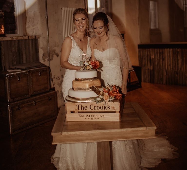 Brides stand in front of their wedding cake and personalised wooden box on their wedding day