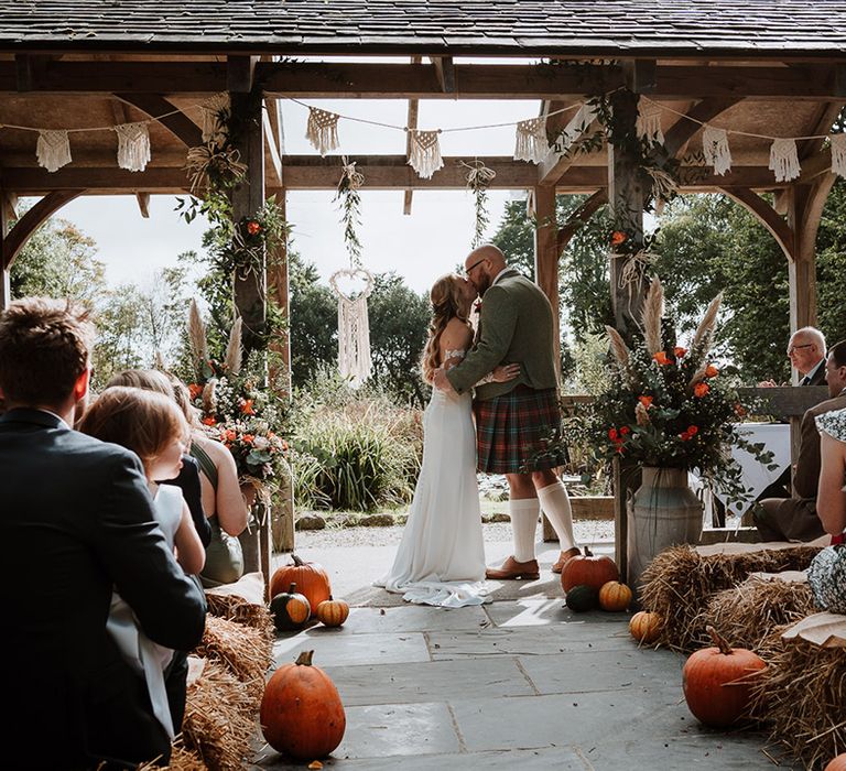 Bride & groom kiss during wedding ceremony with pumpkin decor 