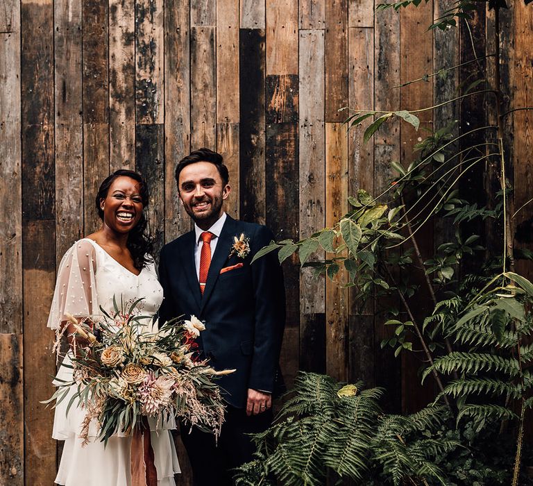 Black bride in a layered skirt and pearl top by Story Of My Dress with her husband in a navy suit at their 100 Barrington wedding in London 