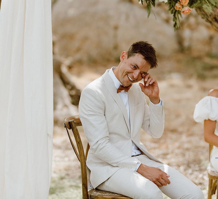 Bride and groom smiling and seated on wooden chairs in outdoors wedding