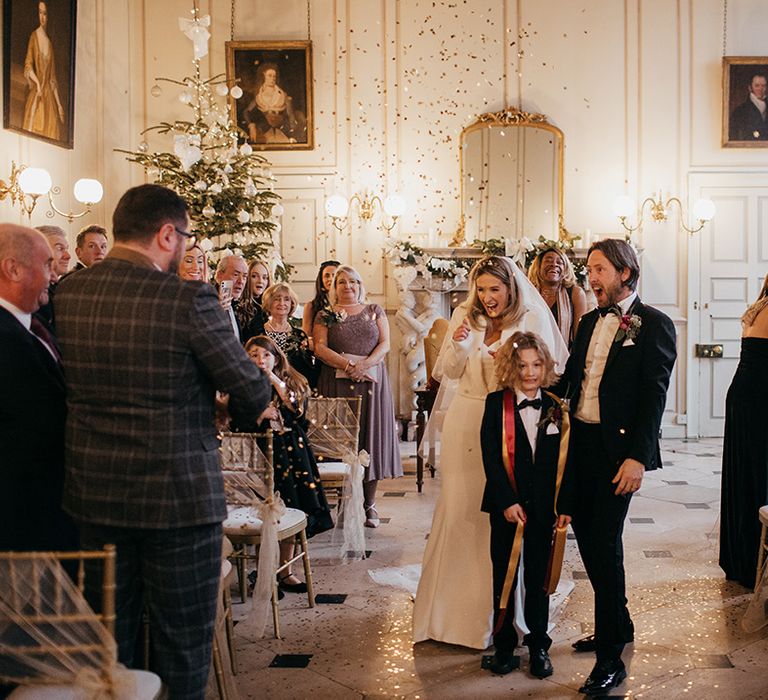 Bride & groom walk down the aisle with their song as confetti cannon explodes around them with gold confetti 