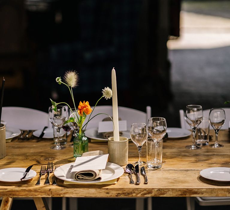 Simple and minimal table setting with orange flowers in vase and white candles