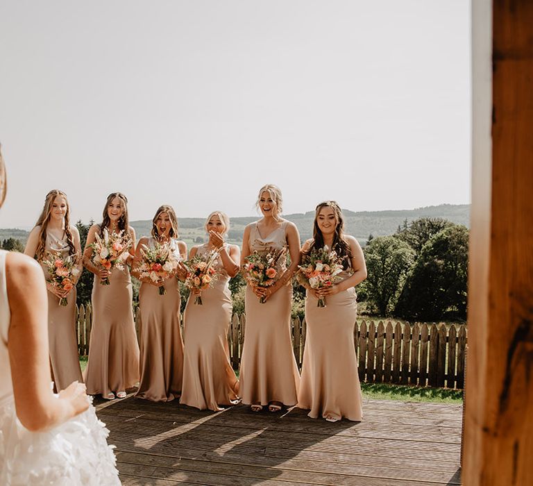 Bridesmaids in matching champagne gold dresses as they get their first look at the bride