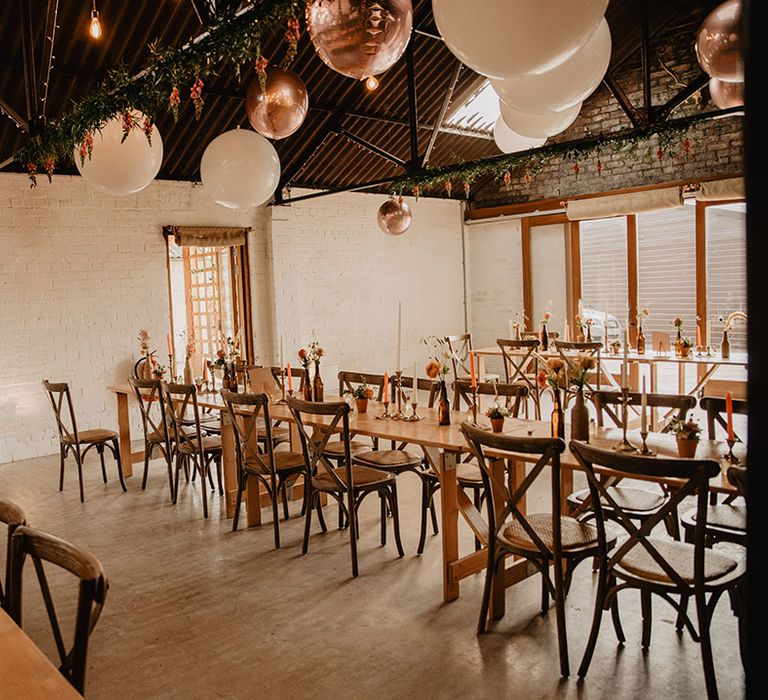 Minimal table setting design withcoloured candles, small potted plants and large white and rose gold balloons for decoration