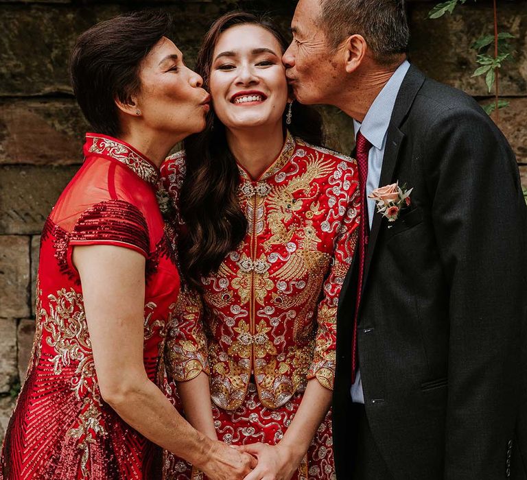 Smiling bride gets a kiss on both of her cheeks from her mother and father on her wedding day 