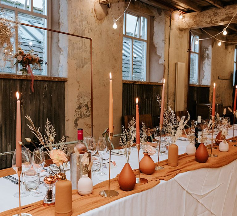 Handpainted terracotta and nude vases with matching coloured candles table setting for industrial wedding venue 