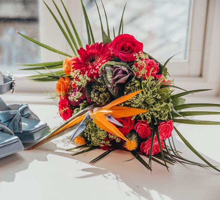 Block platform blue wedding shoes for bride next to bridal bouquet of bright red and orange flowers and foliage