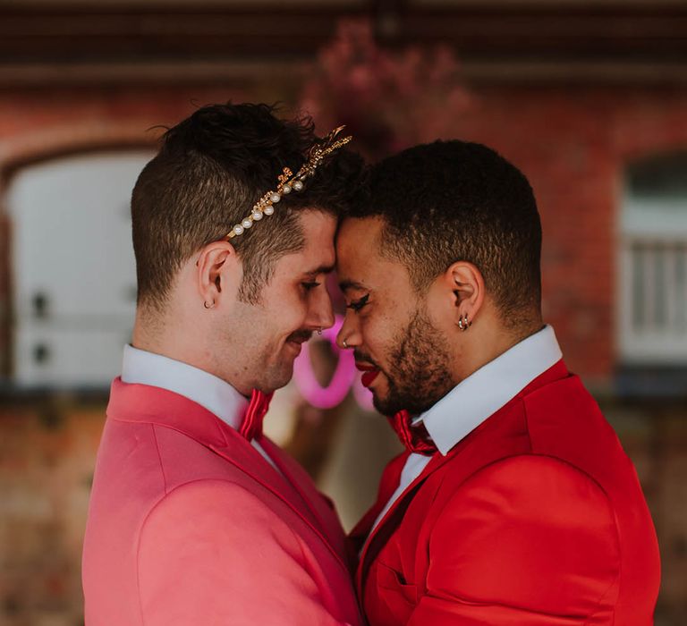 LGBTQI+ couple embracing in pink and red wedding suits 